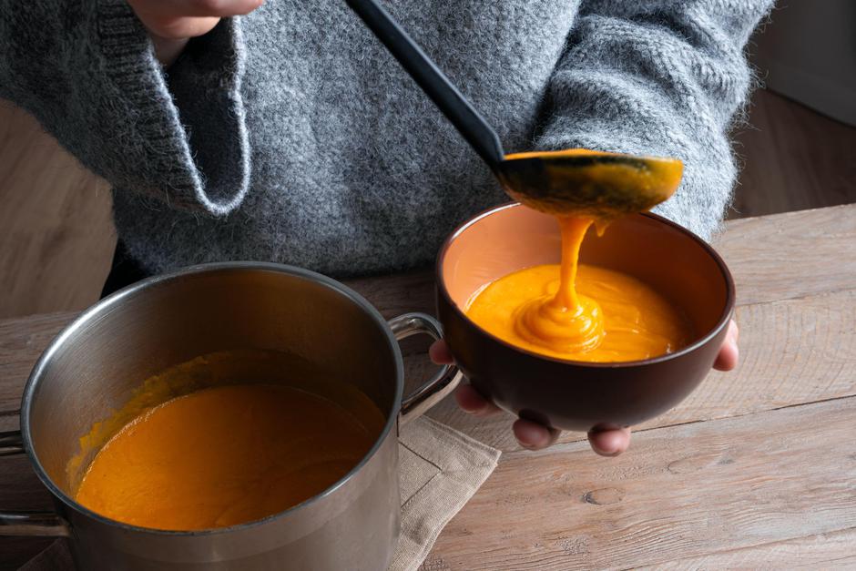 Person's hands ladling pumpkin soup into bowl, wearing knitter sweater. Woman pouring red lentil and vegetable soup. Healthy eating and family comfort | Author: Profimedia